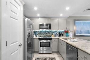 A modern kitchen with stainless steel appliances, a tiled backsplash, and a view of the sea through a window. - Dog Friendly Condo with Gulf Views (Miramar Beach)