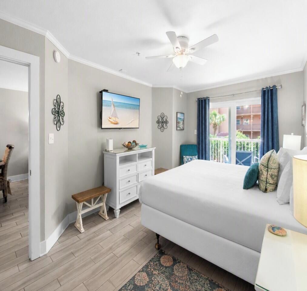 A bedroom with a bed, a nightstand, a dresser, a ceiling fan, and a view of the outside.