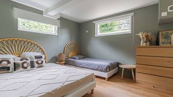 A bedroom with a bed, a chair, a dresser, and two windows.