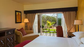 Une chambre d’hôtel avec un lit, deux chaises, un bureau, une lampe, un ventilateur de plafond et une vue sur l’extérieur.