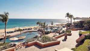 Een resort met een zwembad, ligbedden, palmbomen en uitzicht op de oceaan.
