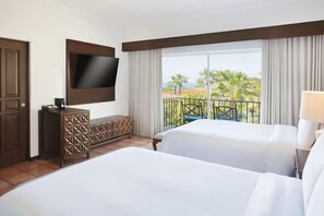 Une chambre d’hôtel avec deux lits, un téléviseur fixé au mur, un balcon avec vue sur les palmiers et une commode en bois.