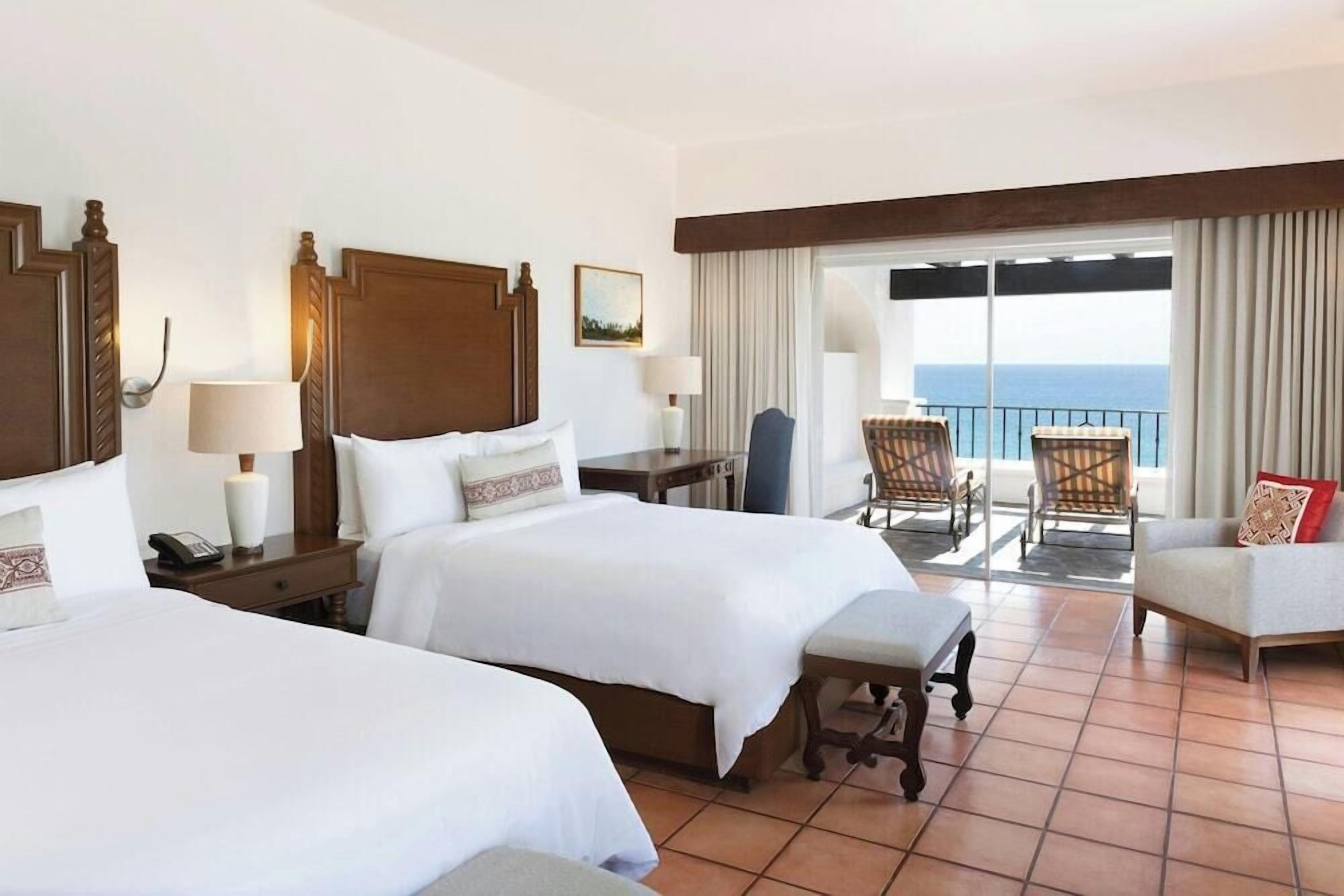 A hotel room with two beds, a balcony with chairs, and a view of the sea.