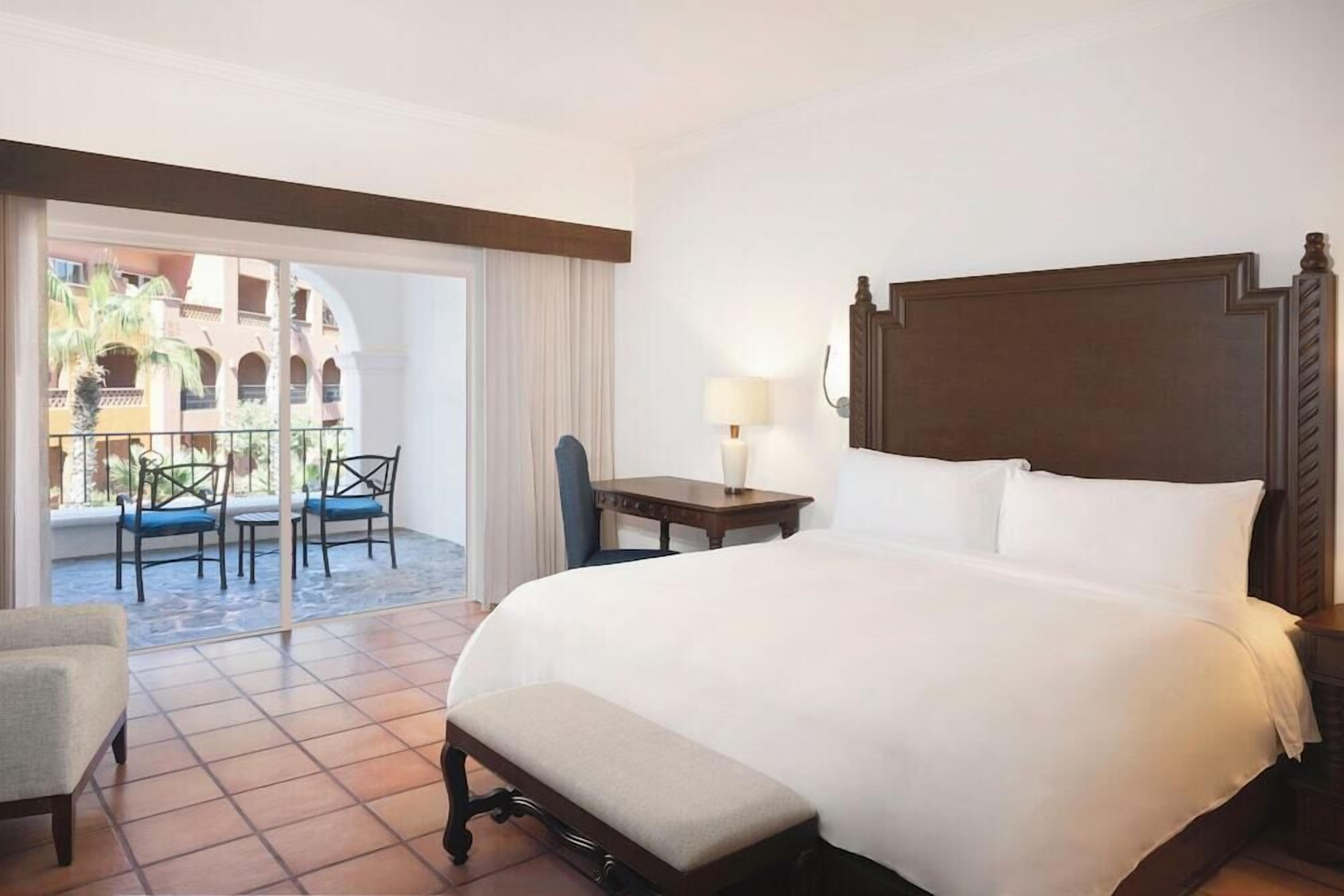 A hotel room with a large bed, a desk, a chair, and a balcony with a view of the courtyard.