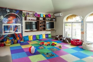 Une salle de jeux avec des tapis en mousse colorés, des jouets et une affiche de Spiderman.