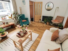 Una sala de estar acogedora con un sofá, una mesa de centro, un sillón azul verdoso y una ventana con plantas en macetas.