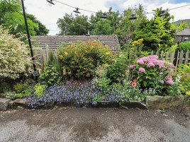 A garden with various plants and flowers, a wooden fence, and a stone wall.