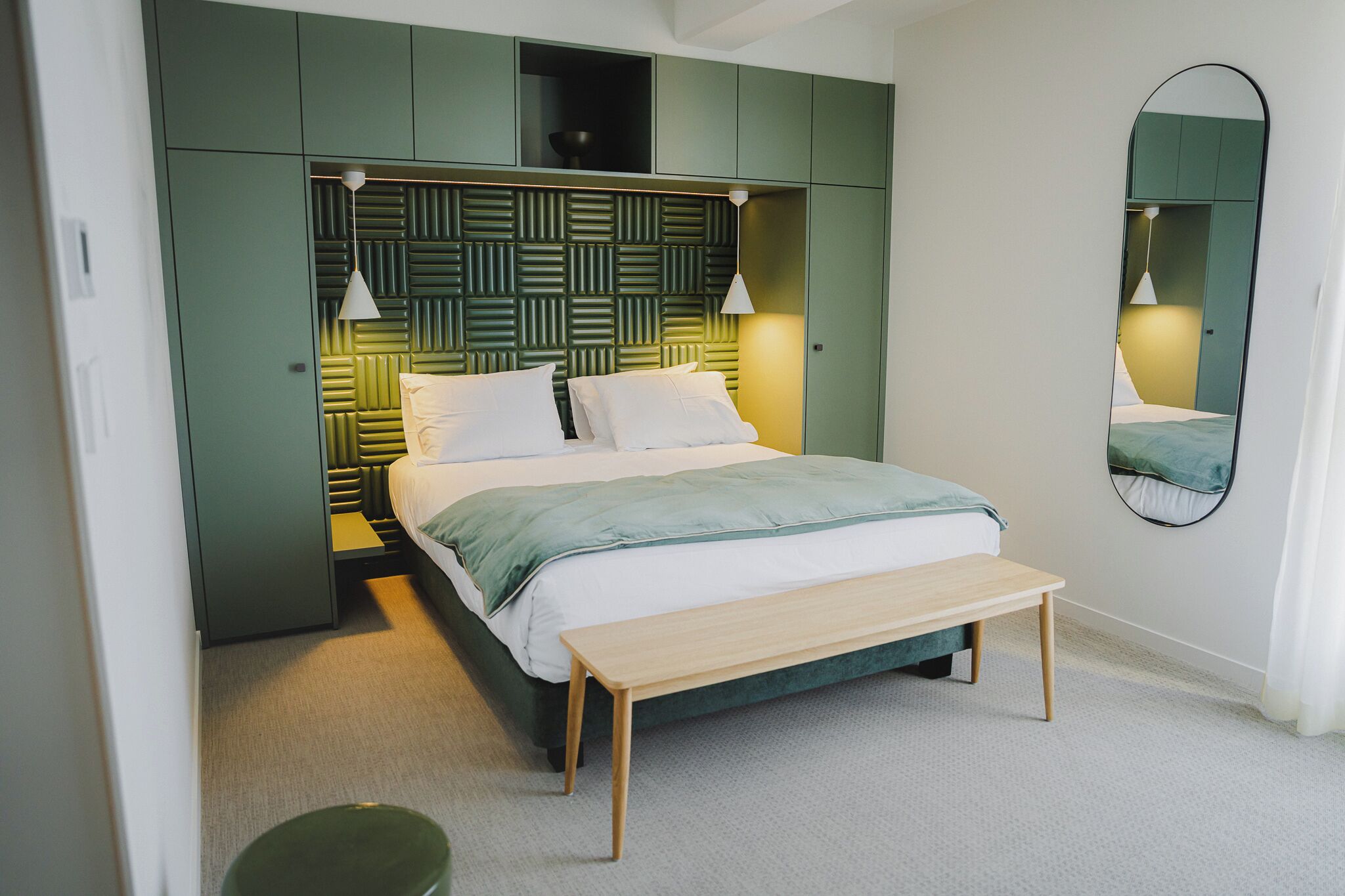 Un dormitorio moderno con cama, mesitas de noche, un banco y un espejo.