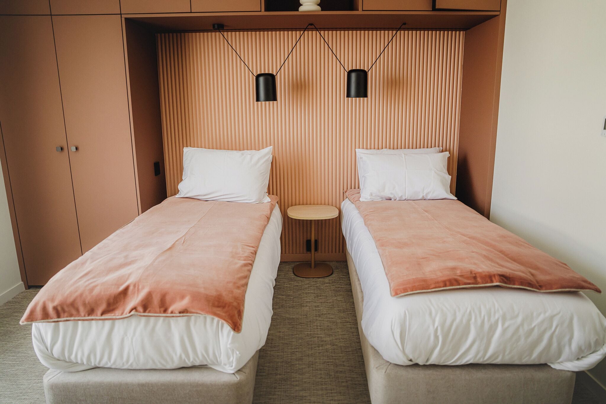 A double room with two beds, a small round table, and a wooden slatted headboard.