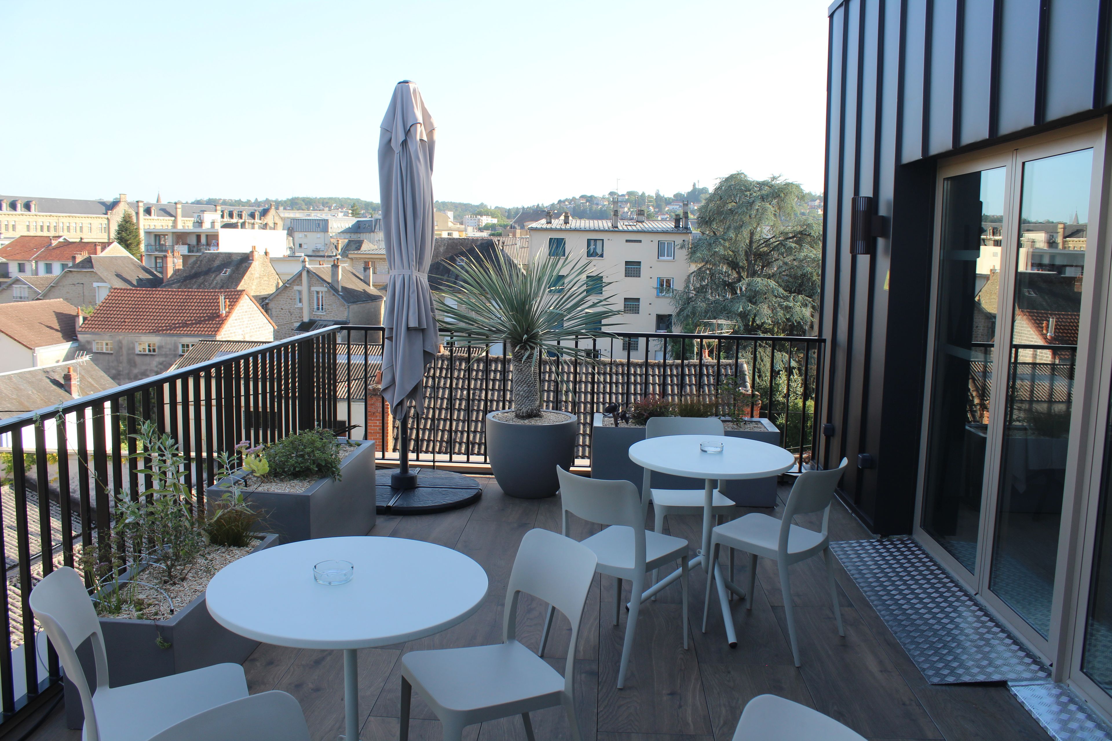 Une terrasse extérieure avec des tables et des chaises, un pot de fleurs et une vue sur le paysage urbain.