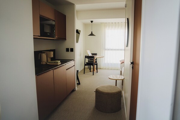 A narrow hallway with a kitchen on the left, a dining area with a table and chairs in the center, and a small round table with a chair on the right.