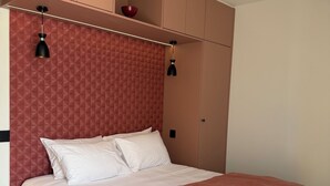 Une chambre à coucher avec un lit, un mur rouge à texture, un pouf gris et des placards intégrés.