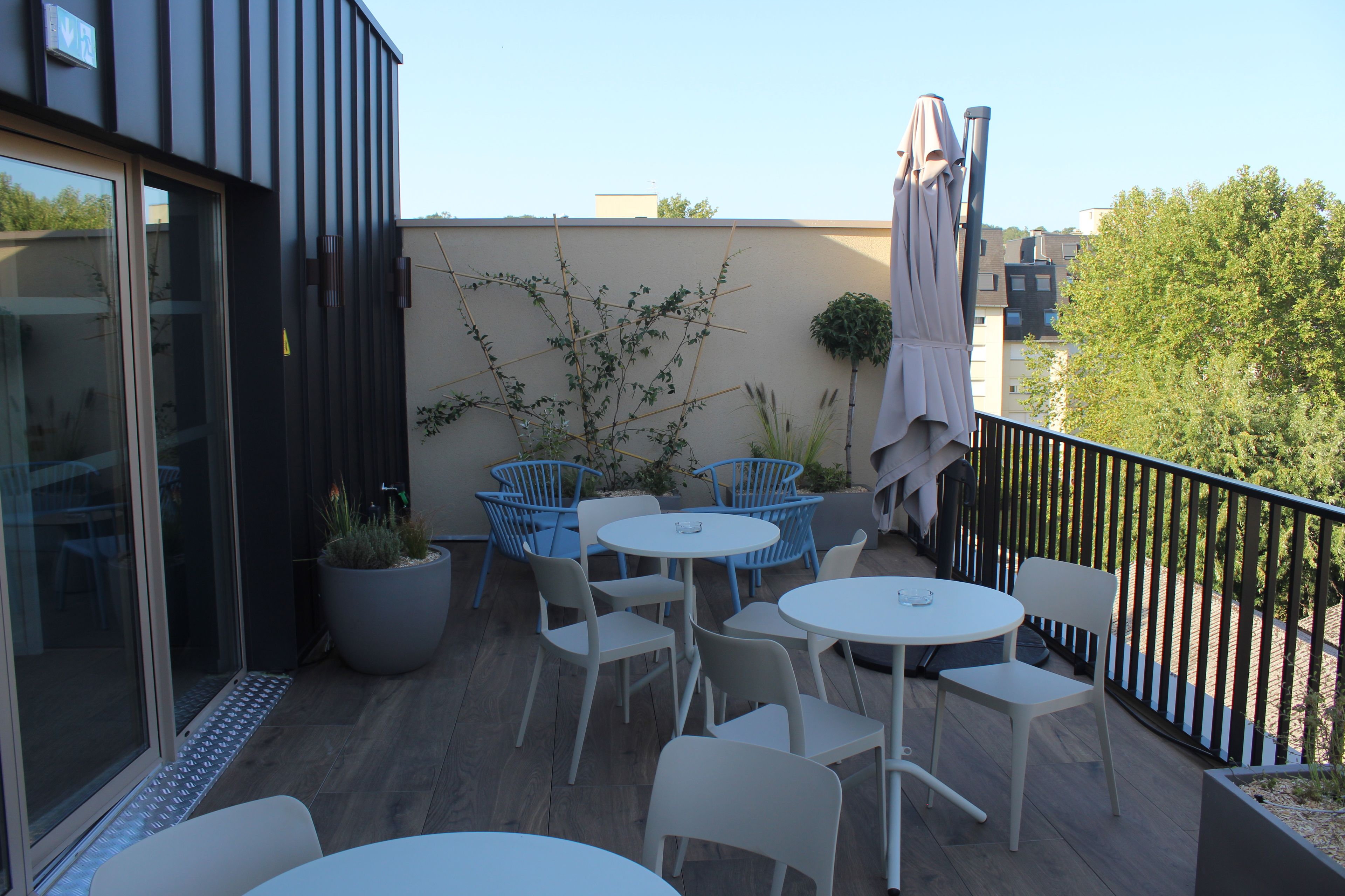A balcony with outdoor seating, including tables and chairs, and a potted plant.