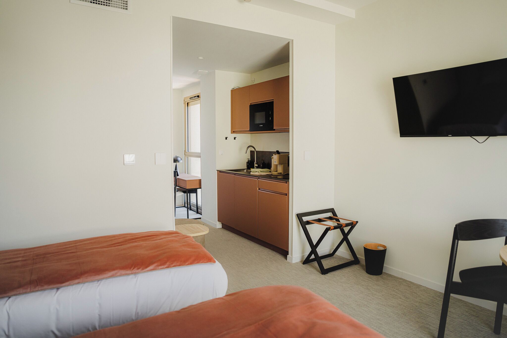 Une chambre d’hôtel avec deux lits, une kitchenette, un téléviseur fixé au mur et une chaise.