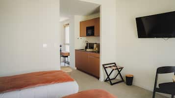 Et hotelværelse med to senge, et tekøkken, et fjernsyn hængt på væggen og en stol.