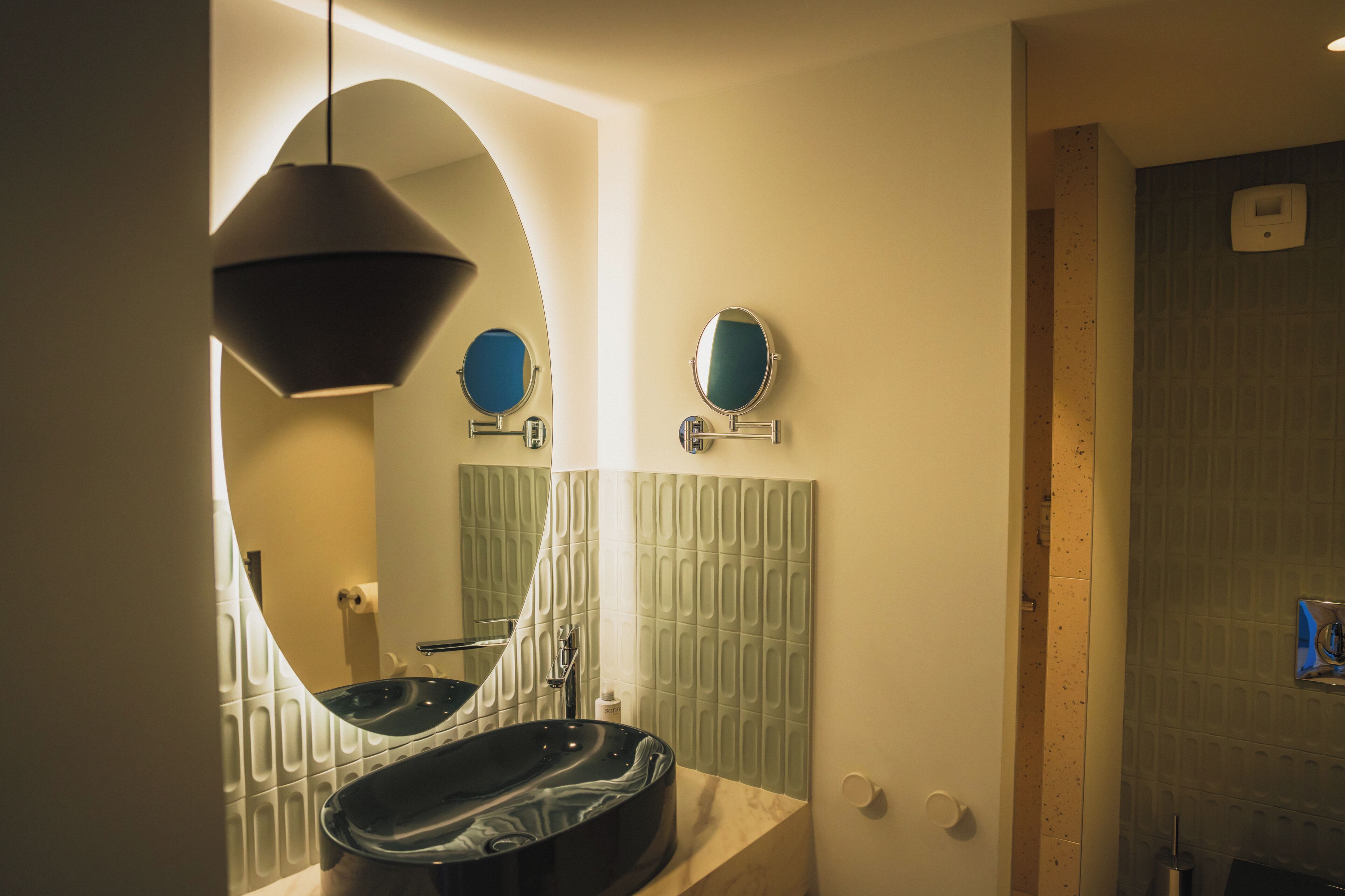 A modern bathroom with a large oval mirror, a round mirror, and a black vessel sink.
