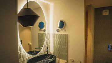 A modern bathroom with a large oval mirror, a round mirror, and a black vessel sink.