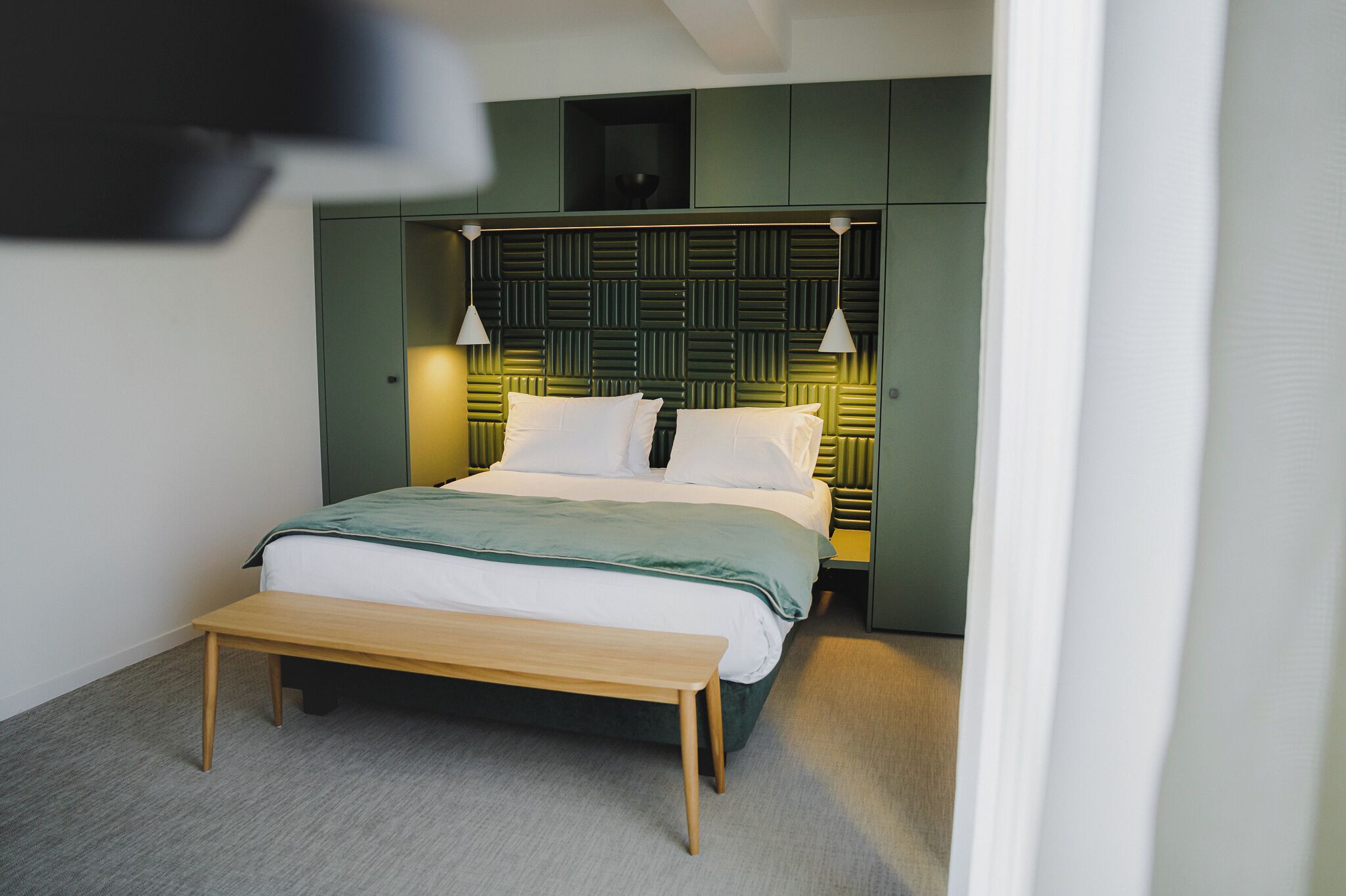 A modern bedroom with a bed, bedside lamps, and a bench.