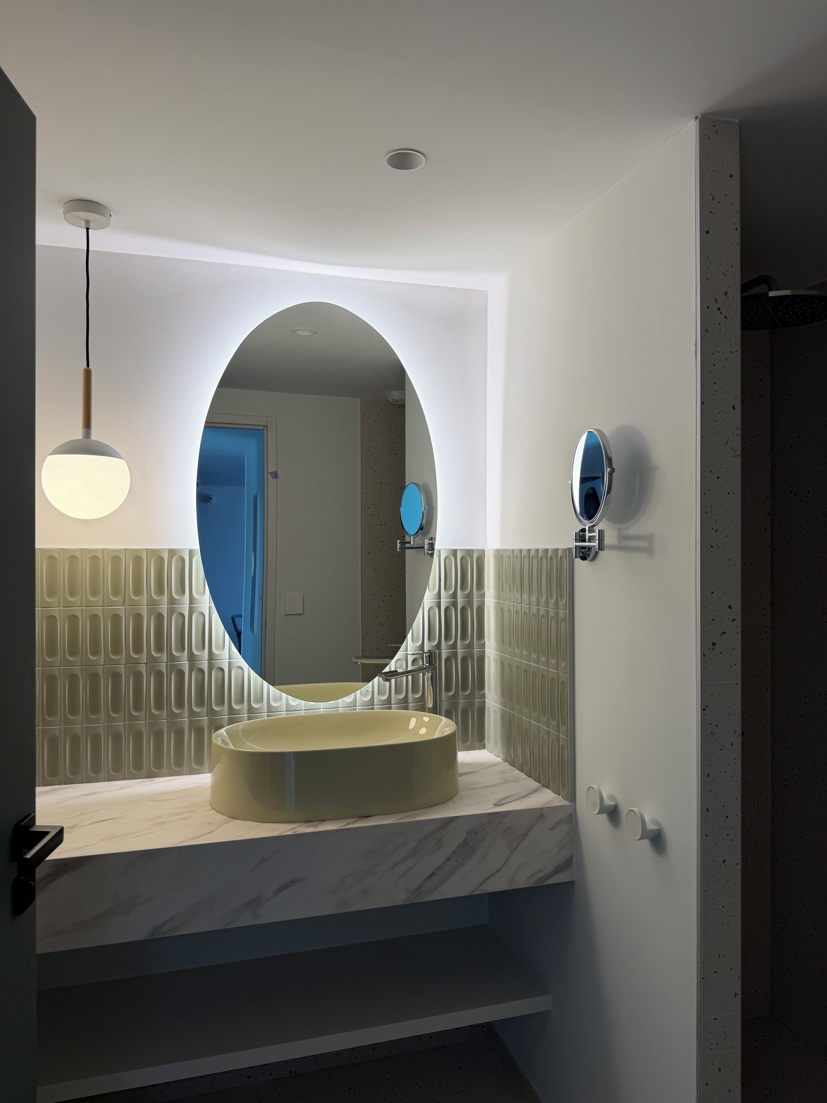 Un bany amb un mirall rodó, un lavabo i un lluminari.