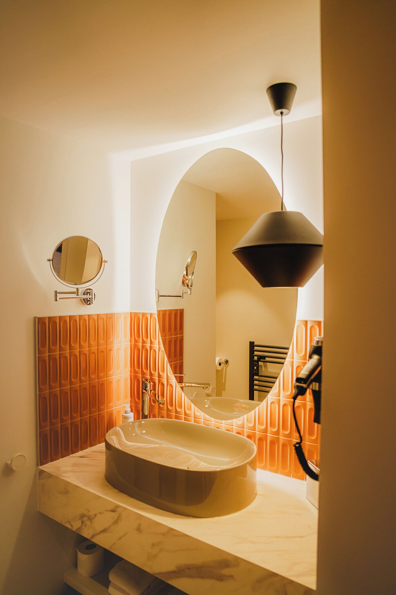 Une salle de bain avec un lavabo en marbre, un miroir rond et un porte-serviettes.