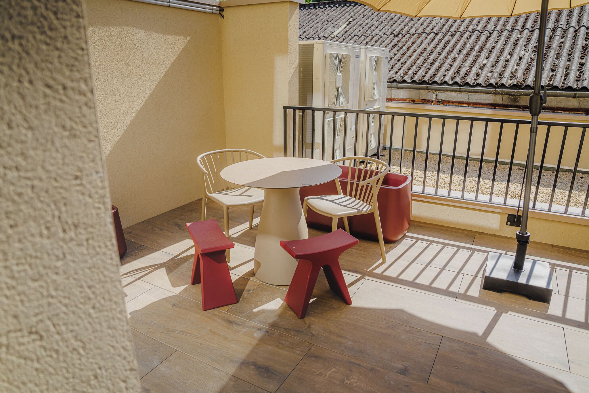 Ein Balkon mit Tisch und Stühlen, eine rote Mülltonne und Blick auf ein traditionelles Ziegeldach.