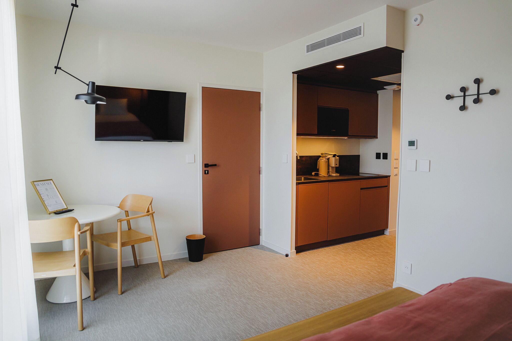 A compact living space with a kitchenette, a dining area with a chair and table, and a television mounted on the wall.