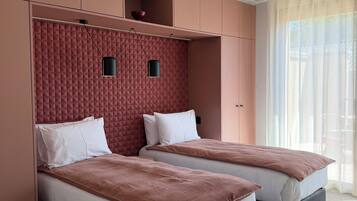 A hotel room with two beds, a built-in wardrobe, and a large window with sheer curtains.