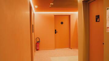 A hotel hallway with carpeted floors, orange walls, and doors marked with numbers.