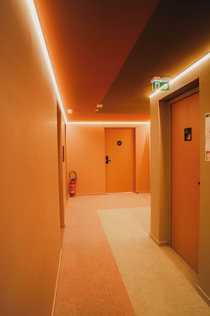 A hotel hallway with carpeted floors, orange walls, and doors marked with numbers.