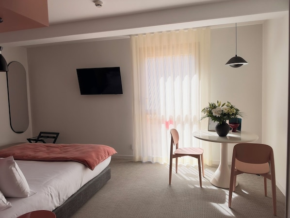 Habitación de hotel con cama, escritorio, silla, televisor y ventana con cortinas.