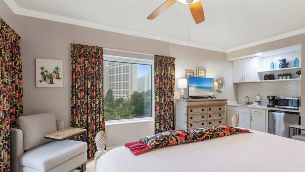 A hotel room with a bed, a chair, a desk, a TV, a kitchen area, and curtains. - Coastal Comfort at TOPSL Summit 309C (Miramar Beach)