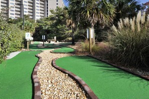 Ein Minigolfplatz mit Kiesweg, grünem Kunikrasen und einer Palme.