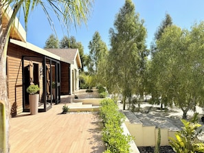 A modern building with wooden siding, a covered porch, and a landscaped garden with trees and shrubs. - Kenz Essia Luxury Countryside Escape Near Tunis (Jedaida)