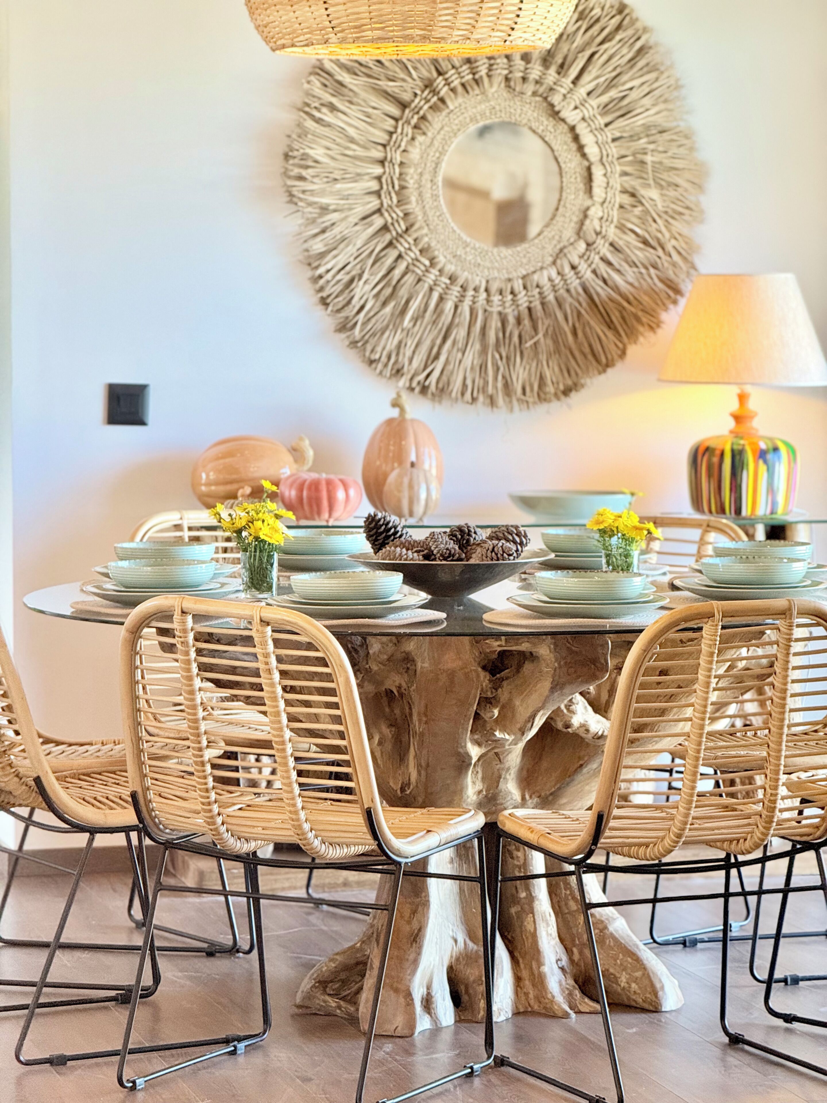 A round dining table with a central mirror, surrounded by wicker chairs, and a rustic tree stump base.