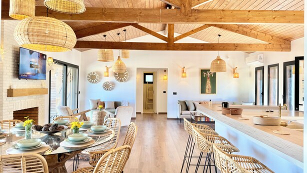 A spacious dining area with a high ceiling, wooden beams, wicker furniture, and a modern kitchen with a large island. - Kenz Essia Luxury Countryside Escape Near Tunis (Jedaida)