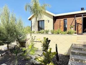 A modern house with a wooden exterior, a large window, and a well-maintained garden with various plants. - Kenz Essia Luxury Countryside Escape Near Tunis (Jedaida)