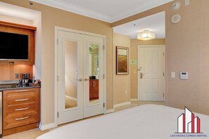 Une chambre d’hôtel équipée d’une kitchenette, d’un grand lit, d’une salle de bain avec douche et d’une porte donnant sur une autre pièce.