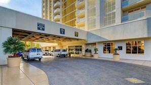 A hotel entrance with a covered driveway, multiple vehicles, and a sign for shuttle services. - MGM Signature-09-704 Jacuzzi Studio (Las Vegas)