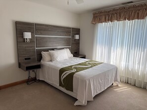 Une chambre d’hôtel avec un grand lit, des lampes de chevet, une tête de lit en bois et des rideaux en voile.