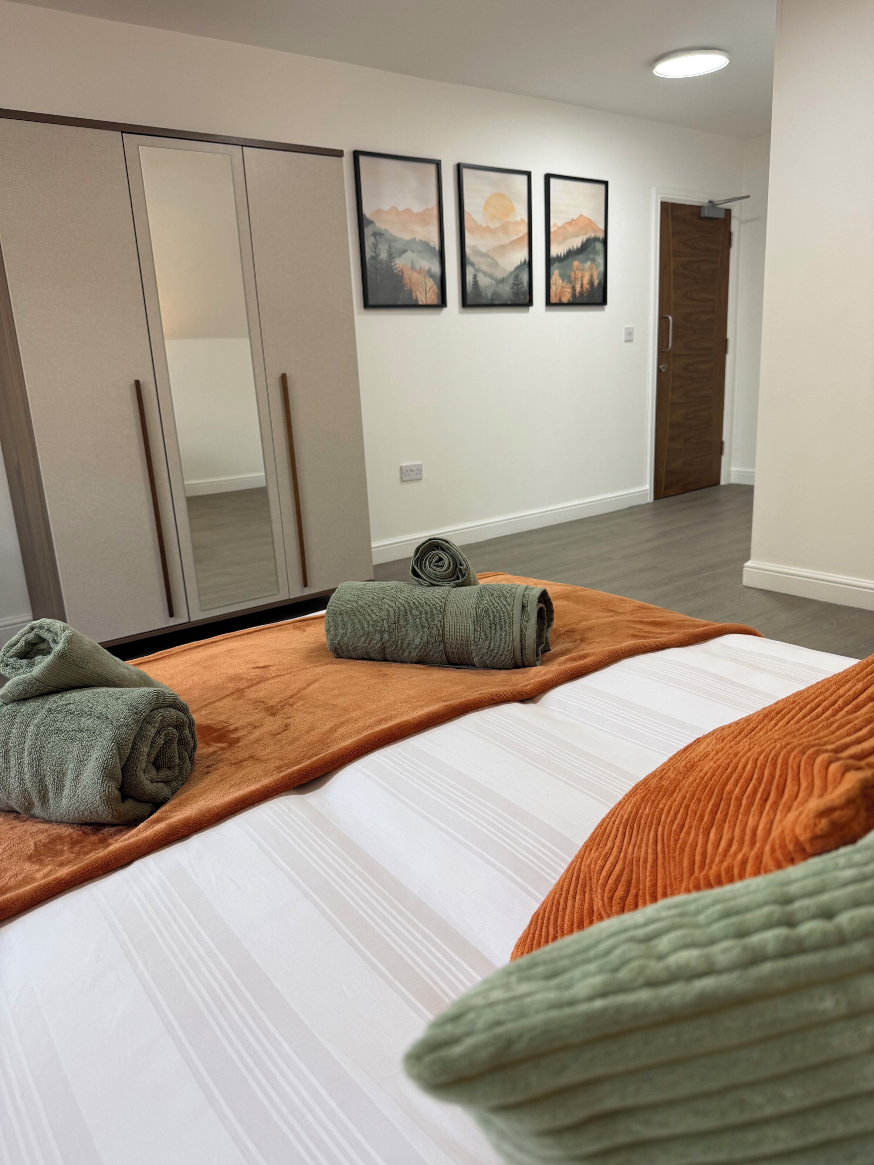 A hotel room with a bed, a large mirror, a wardrobe, and three framed pictures on the wall.
