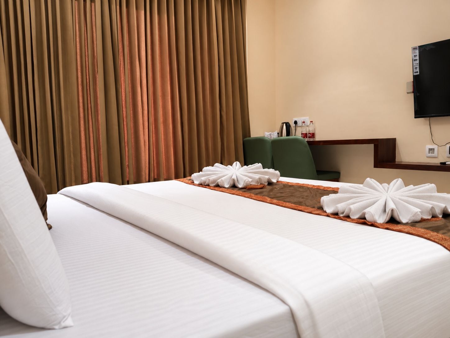 A hotel room with a bed, a desk, a chair, and a television on the wall.
