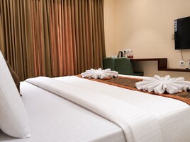 Una habitación de hotel con cama, escritorio, silla y televisor en la pared.