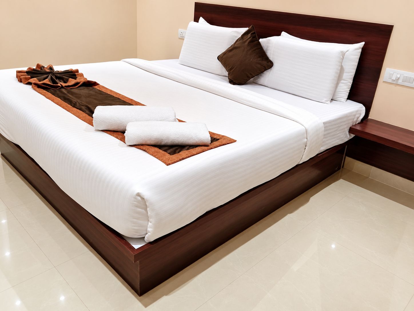Una cama bien hecha con sábanas blancas, un plaid marrón y dos toallas.