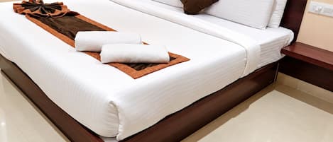 A neatly made bed with white linens, a brown throw, and two towels.