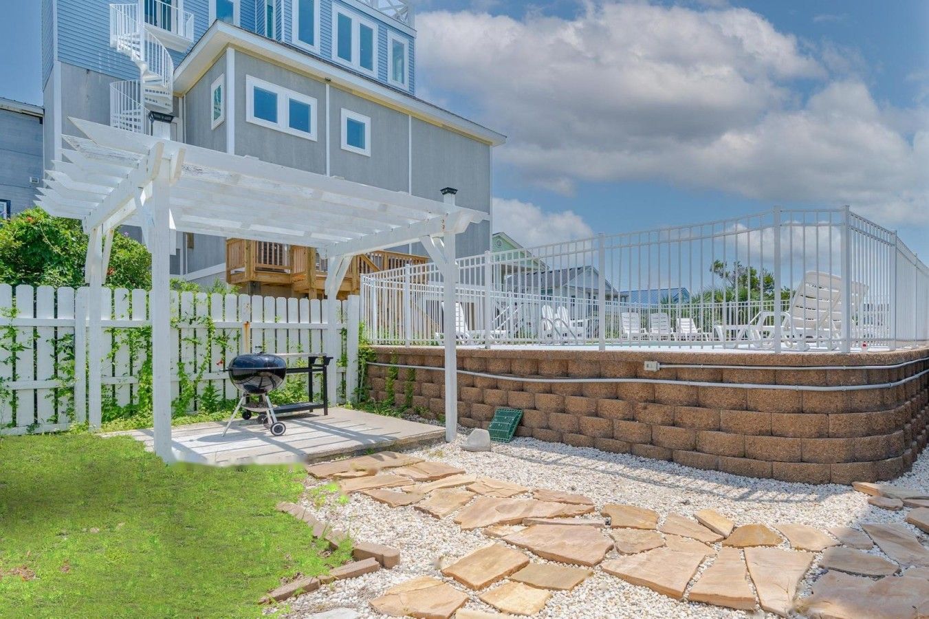 A residential property with a patio, a barbecue grill, a white fence, and a brick wall.