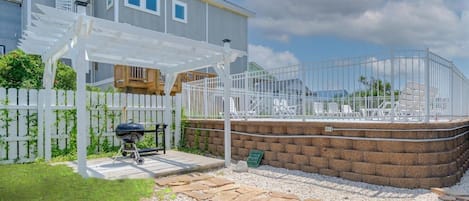 A residential property with a patio, a barbecue grill, a white fence, and a brick wall.