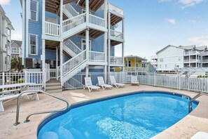 Une piscine dotée de rampes blanches et entourée de chaises longues, le tout bordé d’immeubles à plusieurs étages dotés de balcons.