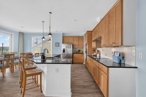 A modern kitchen with wooden cabinets, a central island, and pendant lighting. - Waterview 3BR | Steps to Beach with Pool (Carolina Beach)