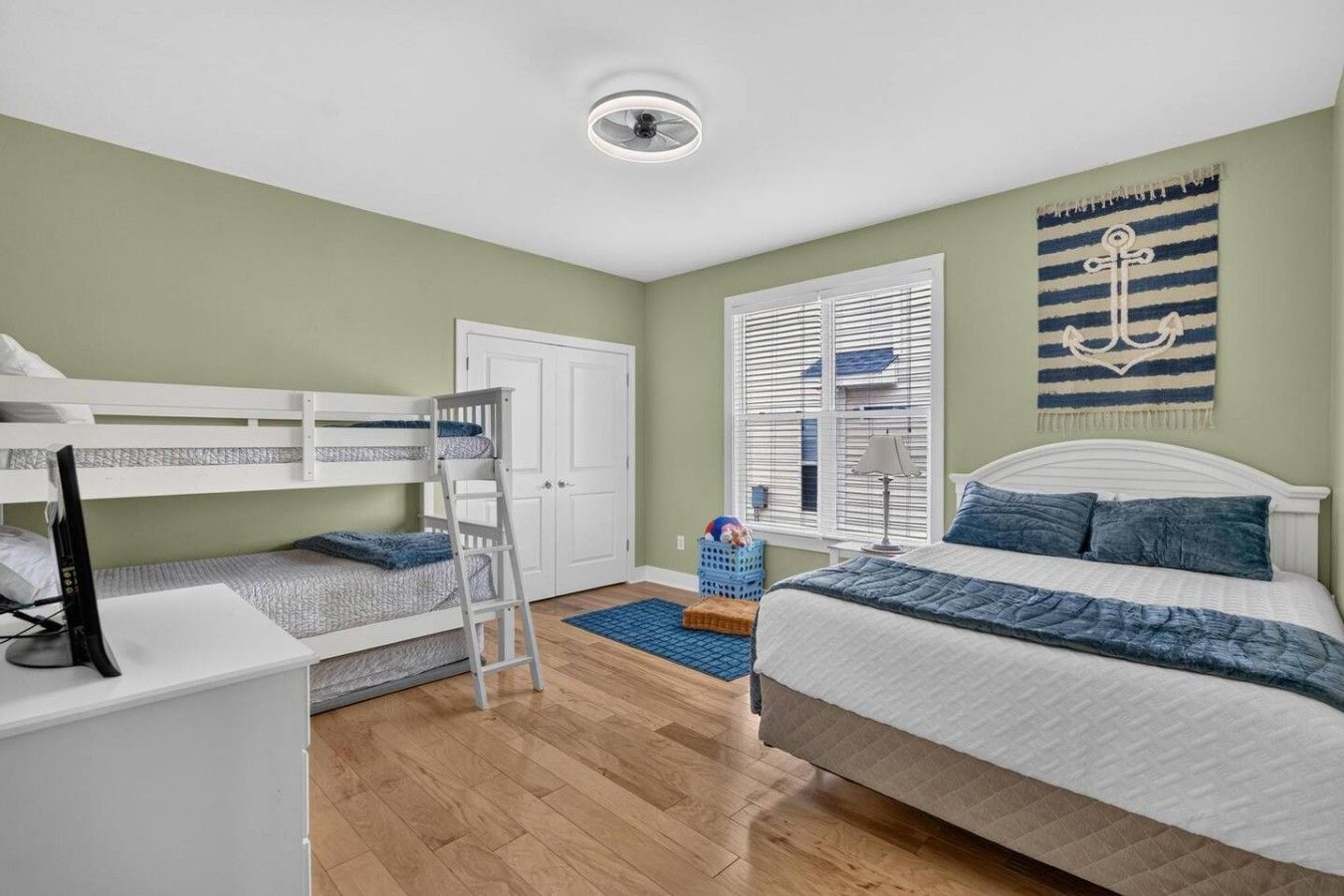 Une chambre avec des lits superposés, un bureau, une armoire, une fenêtre avec des stores et une décoration murale.