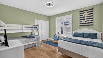 Une chambre avec des lits superposés, un bureau, une armoire, une fenêtre avec des stores et une décoration murale.